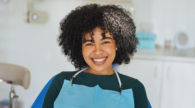 Smiling dental professional wearing blue apron in modern dental office setting.