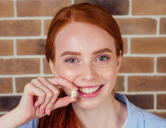 Young woman with red hair smiling while holding dental floss against brick wall background.
