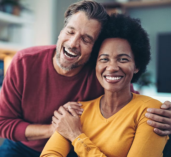 Two smiling people embracing indoors, appearing happy and relaxed in a casual home setting.