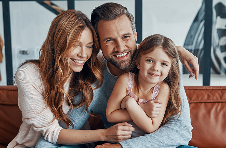 Happy family of three smiling together on couch in home setting.