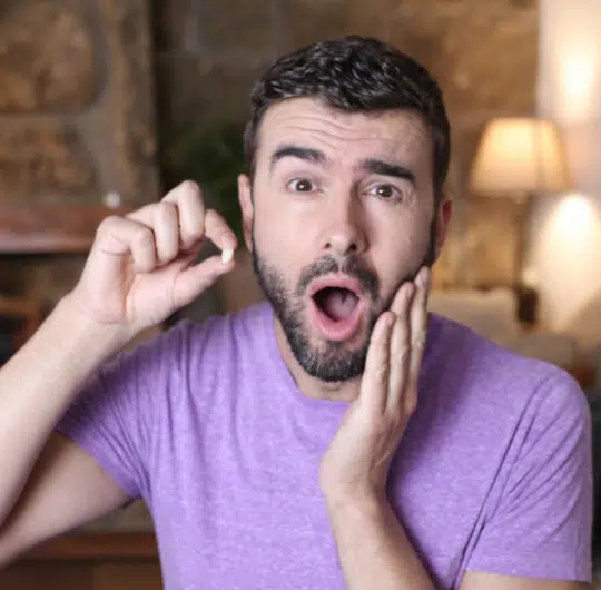 Man in purple shirt touching face with surprised expression in dental office setting.