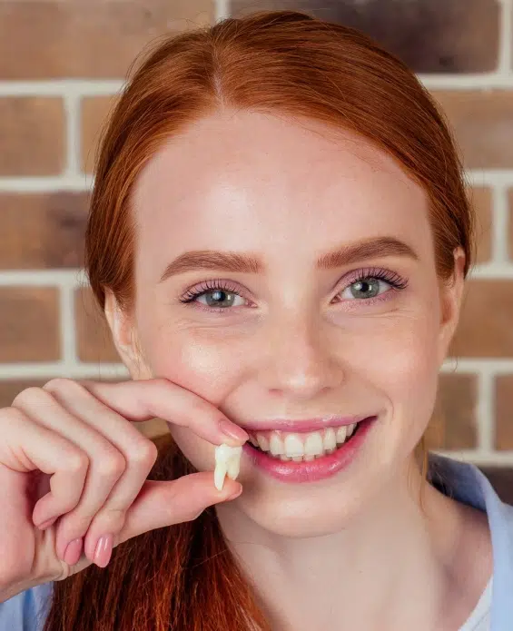 Young woman with red hair smiling while flossing teeth against brick wall background.