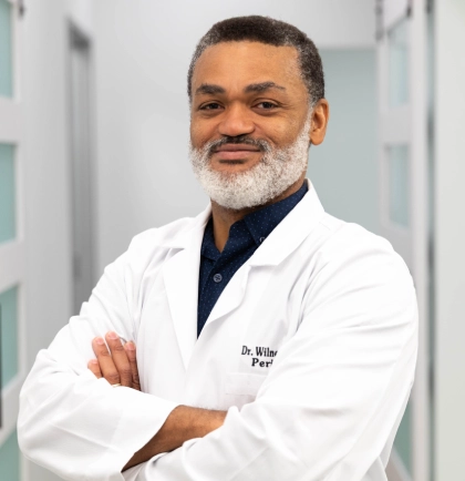 Professional male dentist in white coat with arms crossed in modern dental office setting.